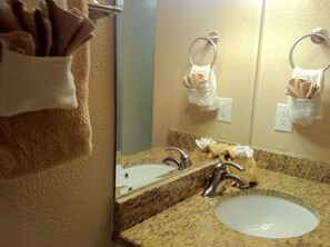 Un baño con lavamanos, espejo, toallero y dispensador de toallas.