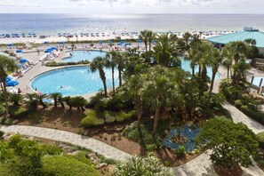 Ein Resort mit einem großen zentralen Pool, mehreren kleineren Pools, Palmen und einem Strandbereich mit Sonnenschirmen.