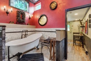 A bathroom with a freestanding bathtub, a round mirror, and a wall-mounted clock.