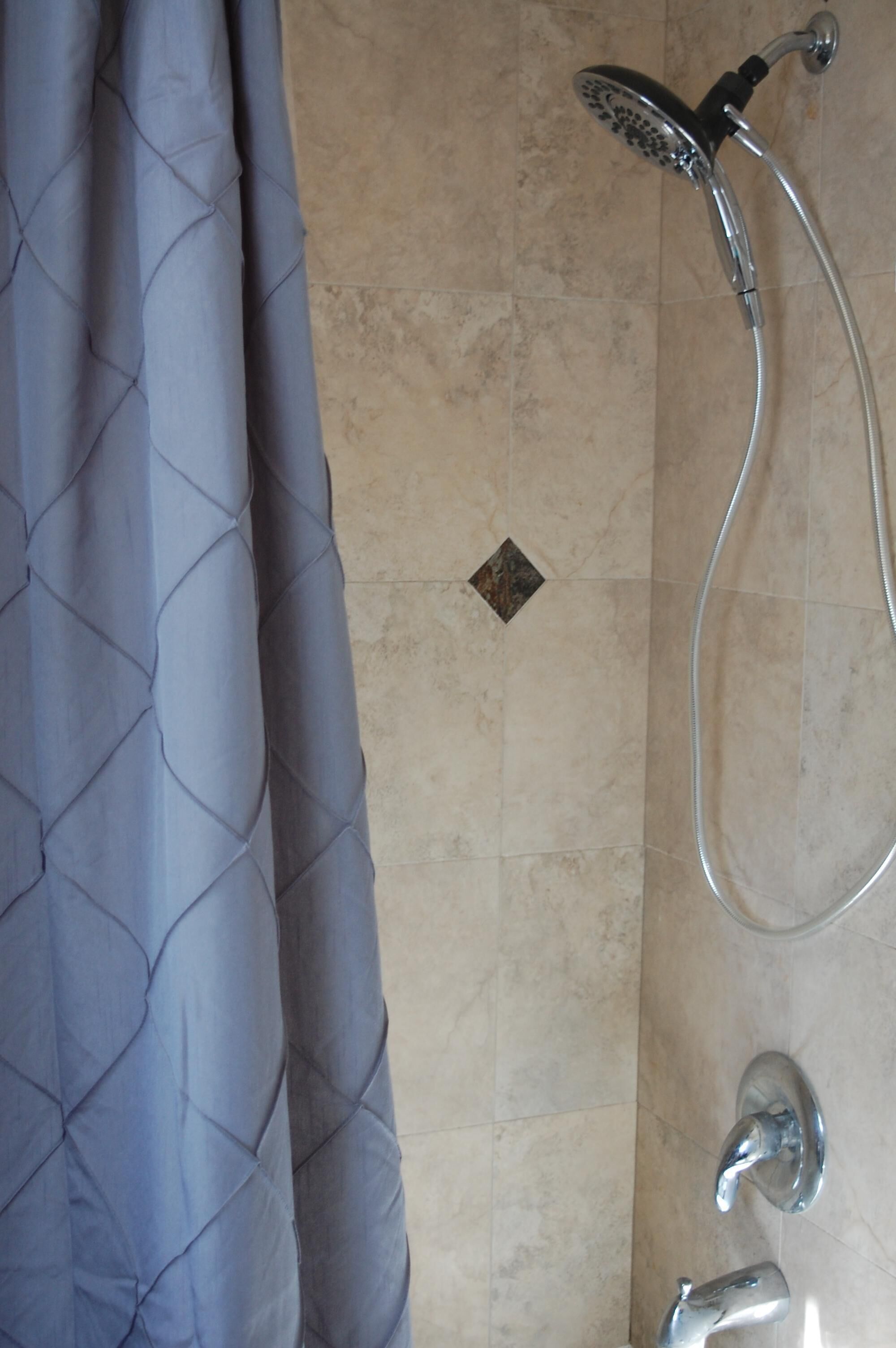 A bathroom with a shower, a tiled floor, and a blue curtain.