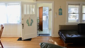 Una habitación con piso de madera, un sofá de cuero negro, una puerta blanca con un cartel de 'Welcome' y una escalera en espiral que conduce a otra habitación.