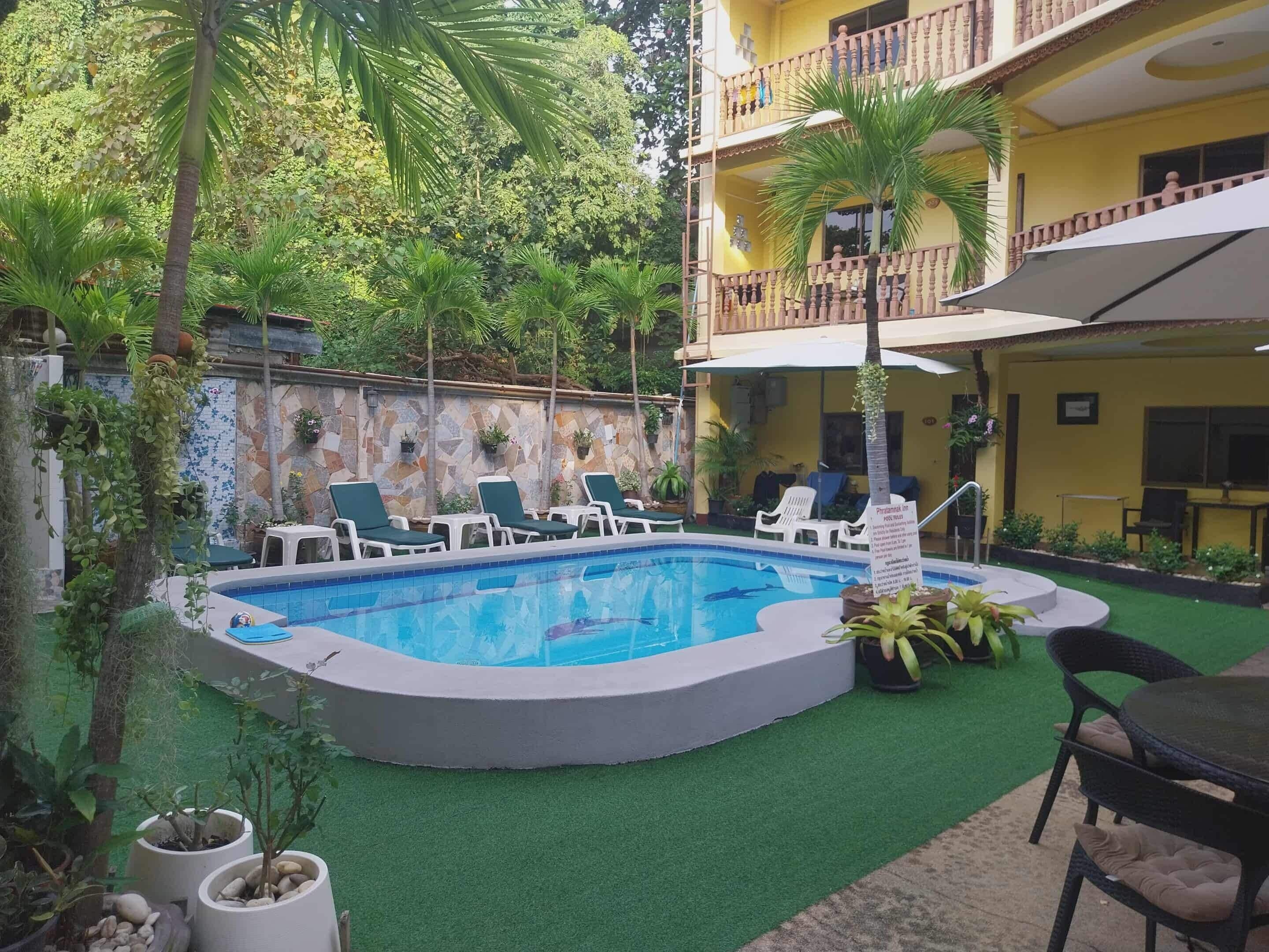 A swimming pool with lounge chairs, a covered seating area, and a building with a balcony.