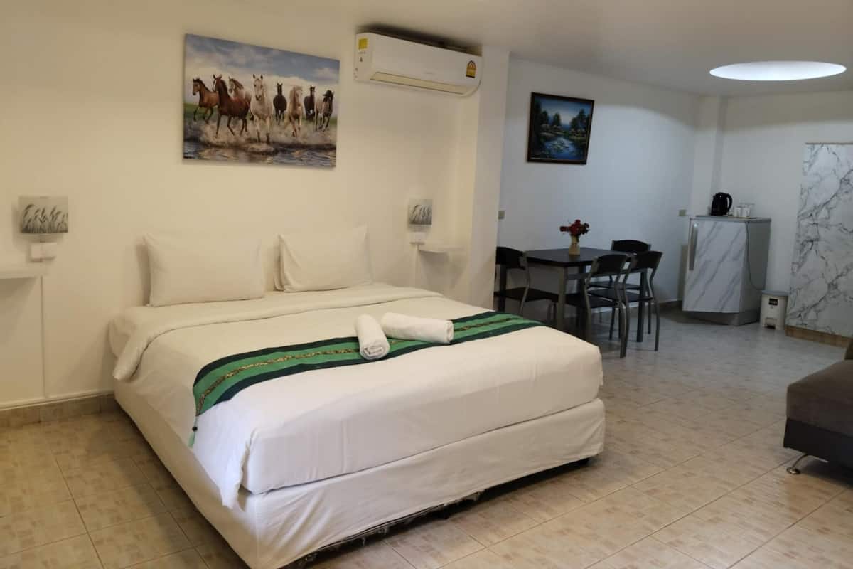 A hotel room with a bed, a desk, chairs, a refrigerator, and a painting on the wall.