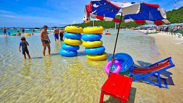 A beach with inflatable rings, a red and blue beach umbrella, and a red and blue beach chair.