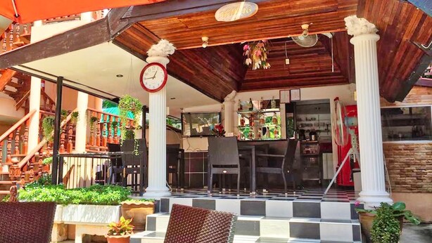 An outdoor seating area with a checkered floor, potted plants, and a bar area with a clock above the entrance. - Phratamnak Inn (Pattaya)