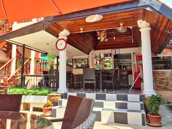 An outdoor seating area with a checkered floor, potted plants, and a bar area with a clock above the entrance. - Phratamnak Inn (Pattaya)
