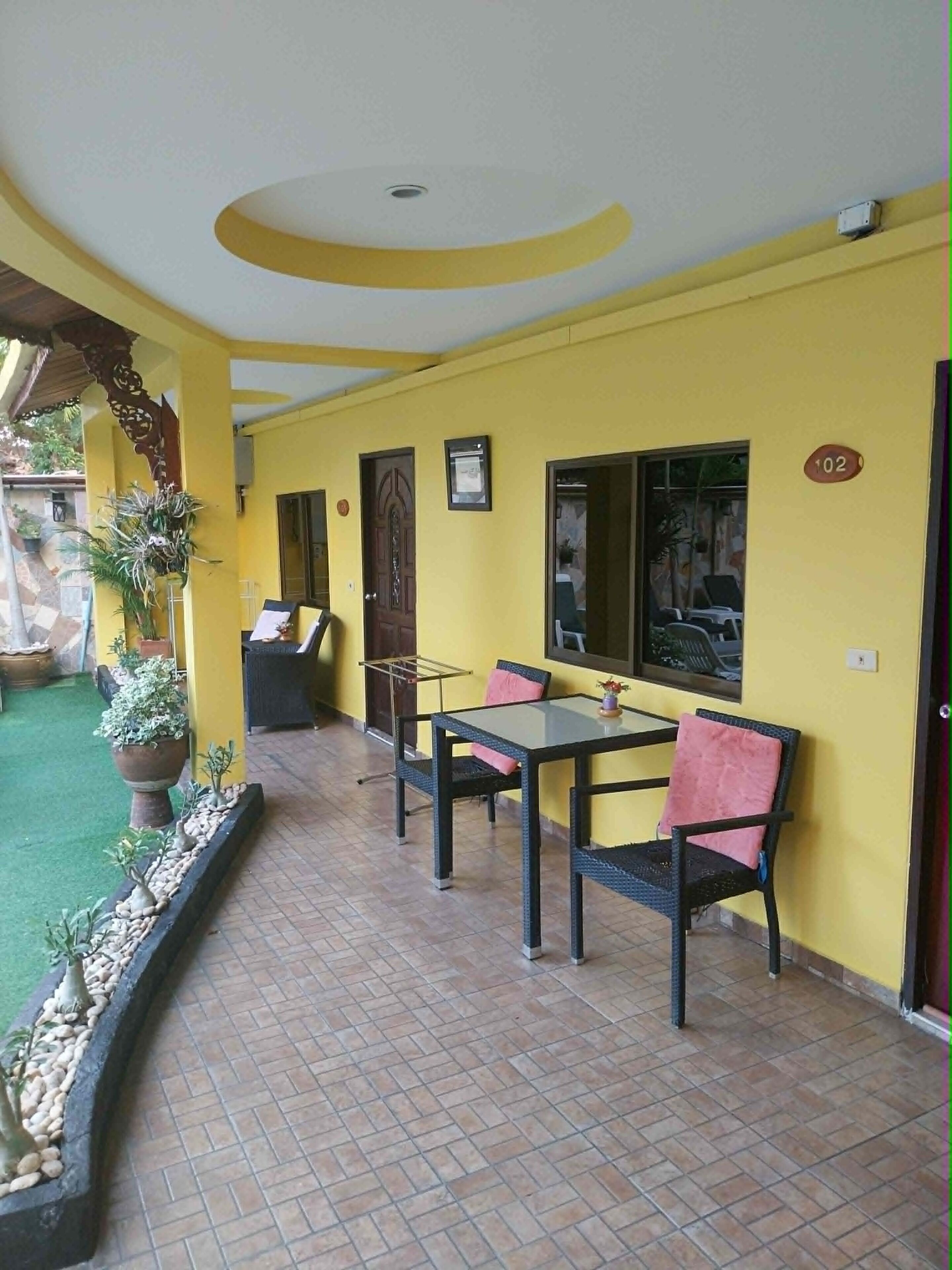 Una habitación con paredes amarillas, piso de baldosas, una mesa con sillas, una puerta y un ventanal.