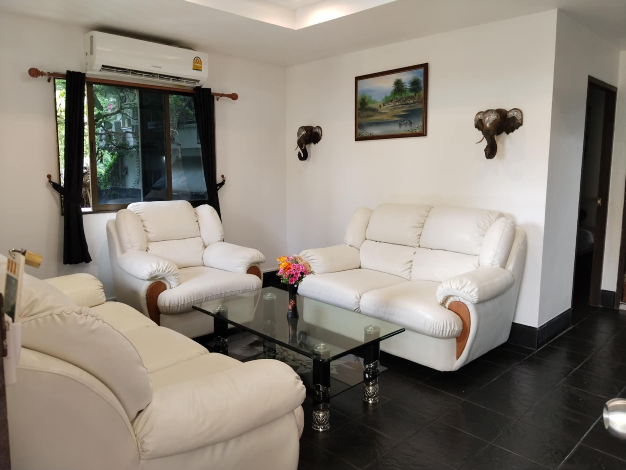 Una sala de estar con dos sofás de cuero blanco, una mesa de centro de vidrio y un cuadro en la pared.