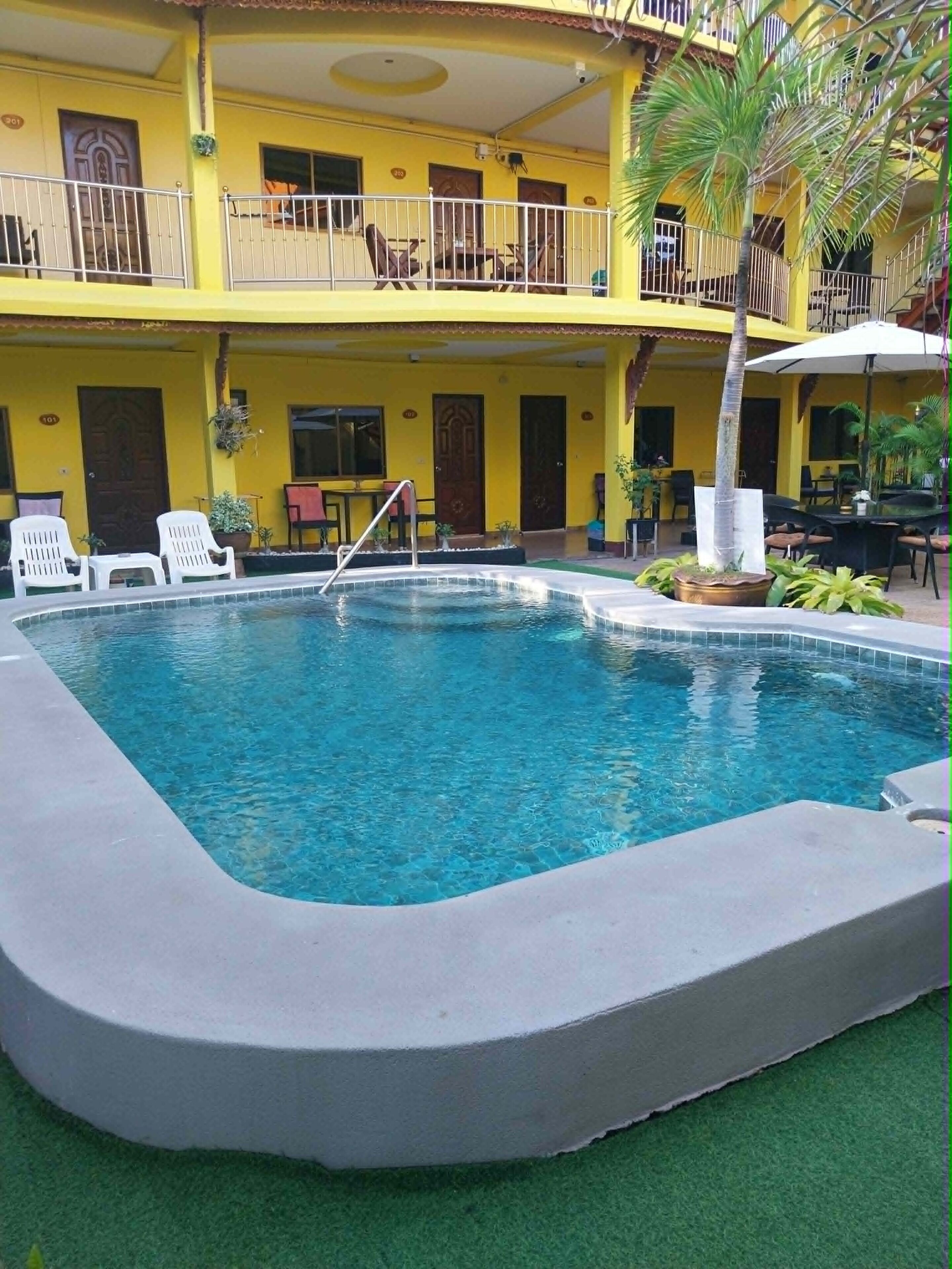 Uma piscina com um deck ao redor, uma área de estar coberta ao ar livre e um edifício com várias varandas.