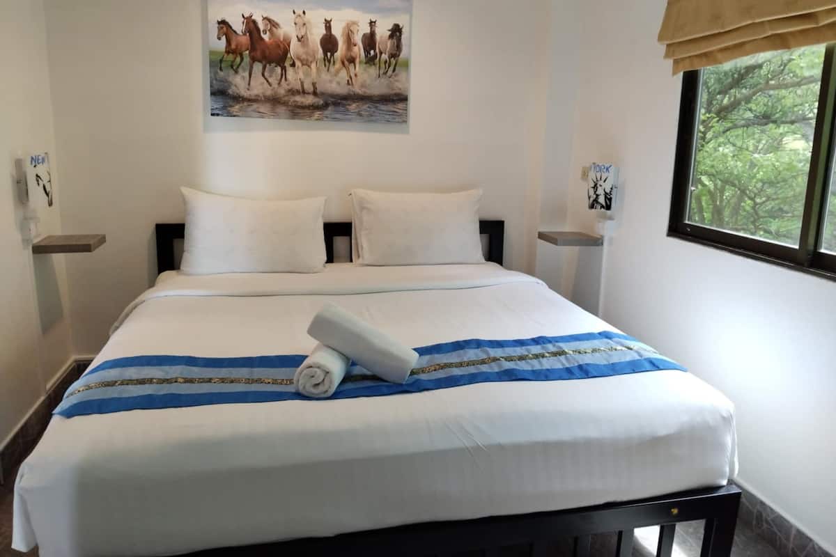 A neatly made bed with a blue and white striped blanket, white pillows, and a rolled towel on the bed. There is a painting of horses on the wall above the bed.