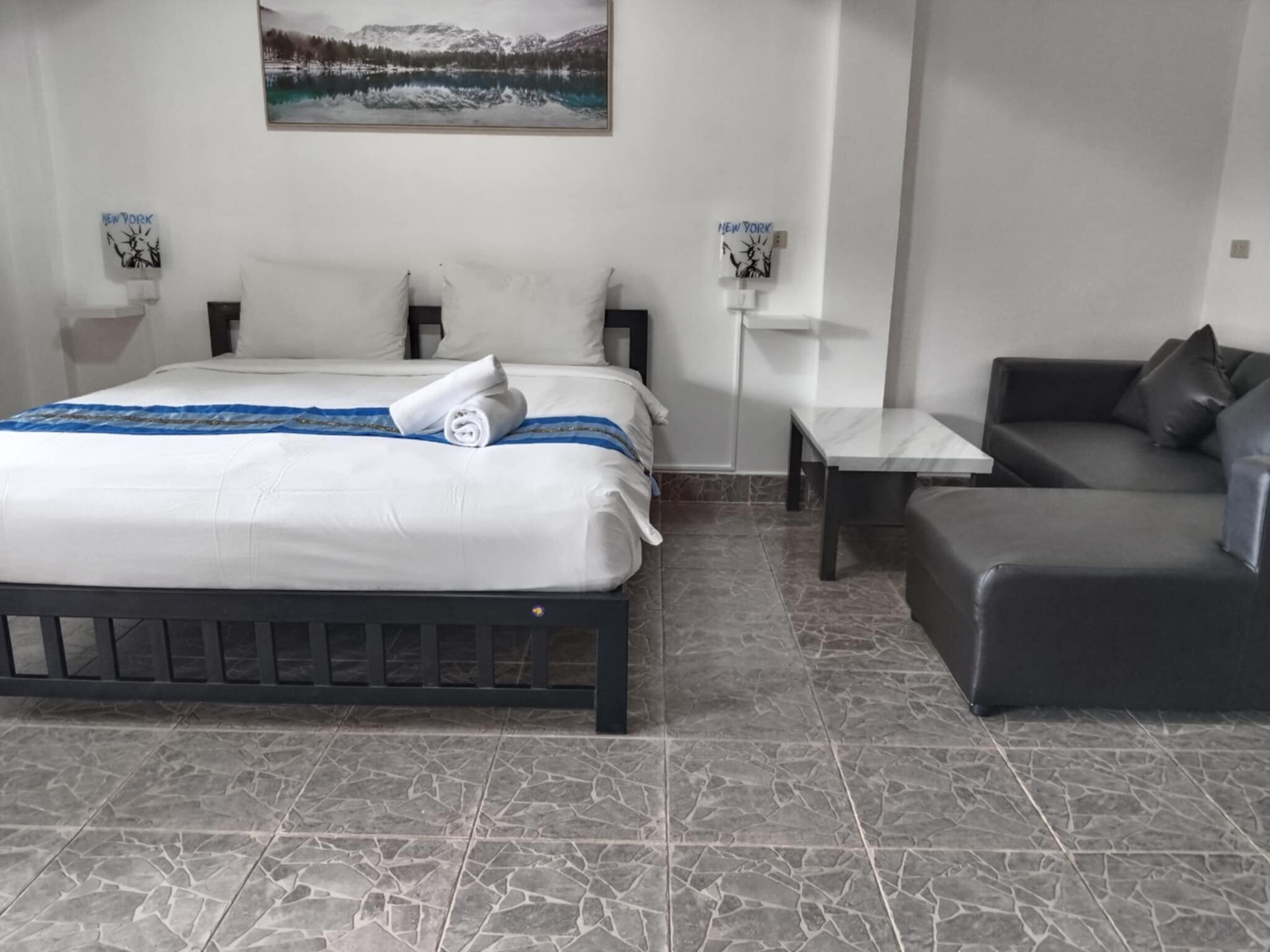 A hotel room with a bed, a sofa, a small table, and a painting on the wall.