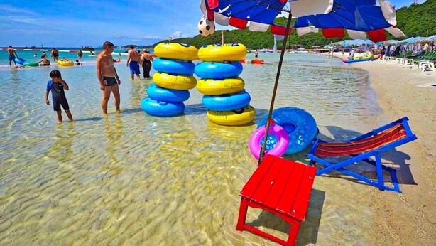 A beach with clear shallow water, inflatable rings, a red and blue beach chair, and a Canadian flag. - Phratamnak Inn (Pattaya)