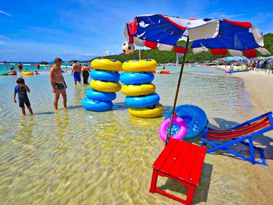 Una playa con agua clara y poco profunda, flotadores, una silla de playa roja y azul, y una bandera canadiense.
