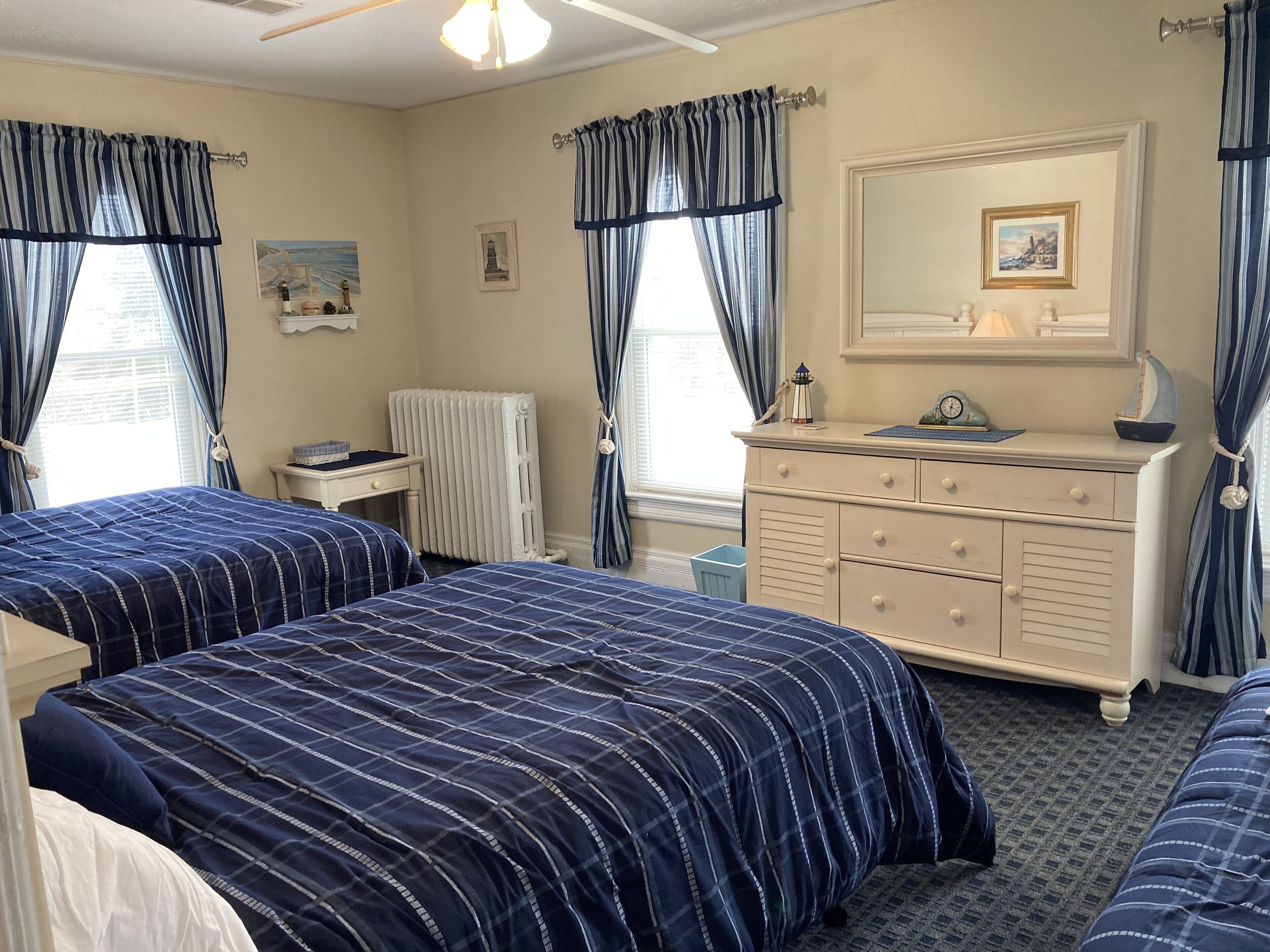 Quarto com duas camas, cômoda, radiador e janela com cortinas.