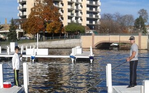Un quai où se trouvent deux personnes en train de pêcher, un pont et un bâtiment en arrière-plan.