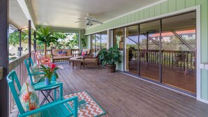 A covered outdoor patio with wooden flooring, turquoise chairs, and a ceiling fan.