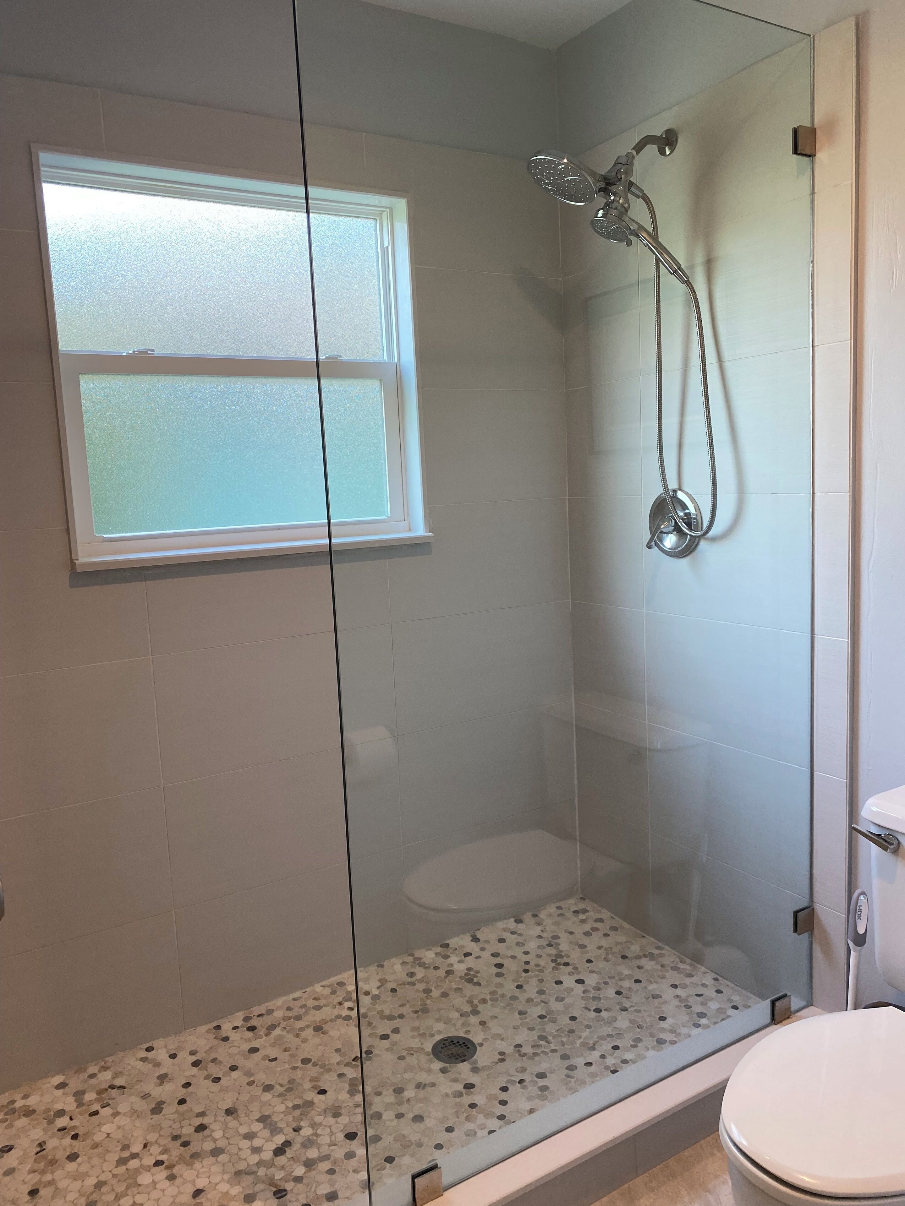 A modern bathroom with a glass-enclosed shower, a toilet, and a small window.