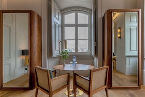 A dining area with a round table, two chairs, a vase with flowers, and a window with a view of buildings.