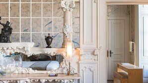 An ornate room with a fireplace, a mirror with a decorative arch, and a wooden bench. - Verride Palácio Santa Catarina (Lisbon)