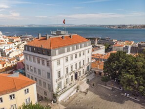 A historic building with a red-tiled roof, a flagpole, and a view of the sea. - Verride Palácio Santa Catarina (Lisbon)