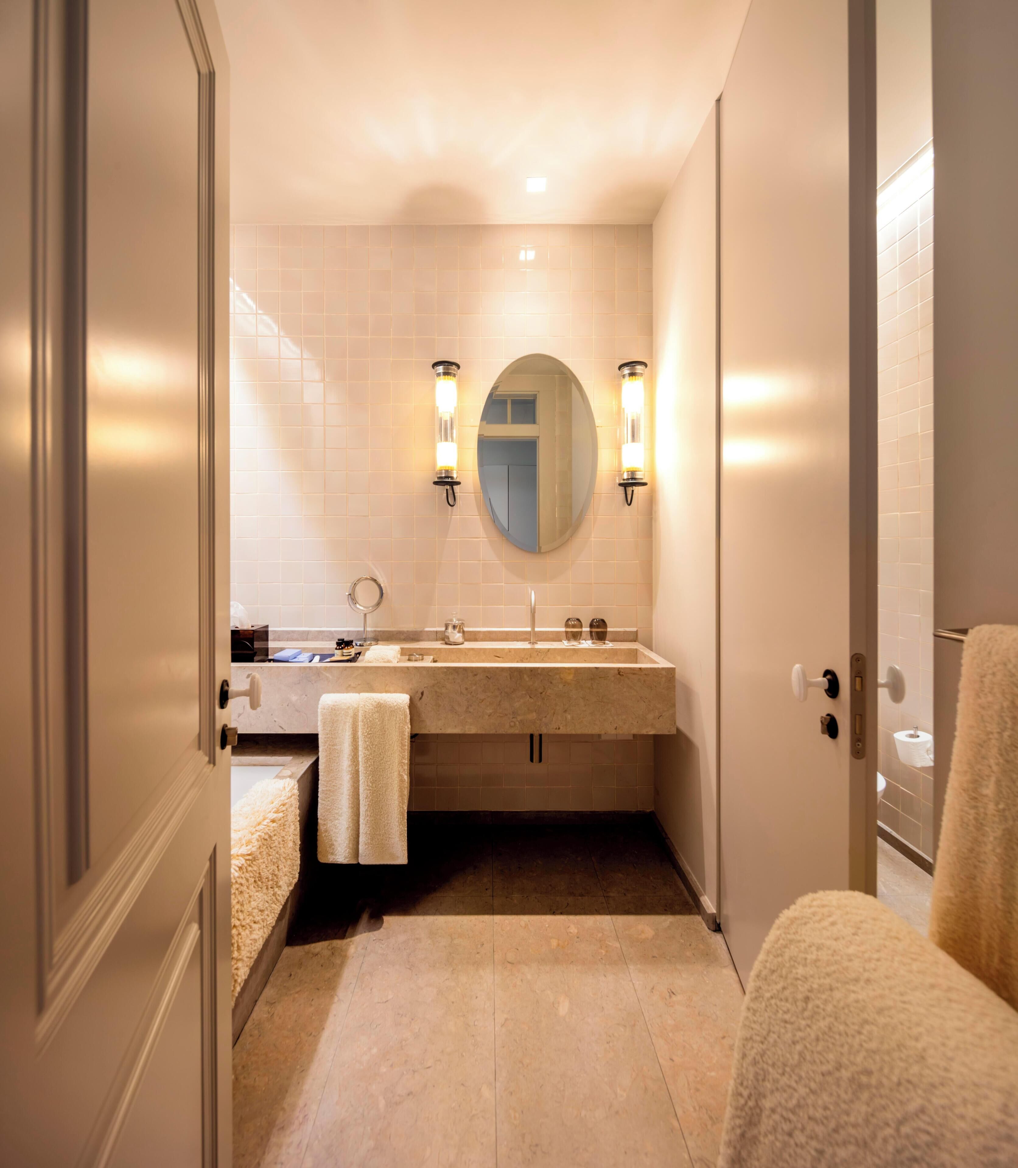 Une salle de bain moderne avec un lavabo en marbre, deux appliques murales, un miroir rond et une serviette posée sur le comptoir.