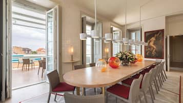 Uma área de jantar moderna com uma mesa oval grande, cadeiras acolchoadas vermelhas e vista para uma piscina.