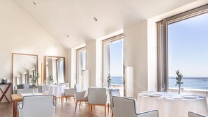 A spacious dining area with high ceilings, large windows offering a view of the sea, and modern furniture. - Verride Palácio Santa Catarina (Lisbon)