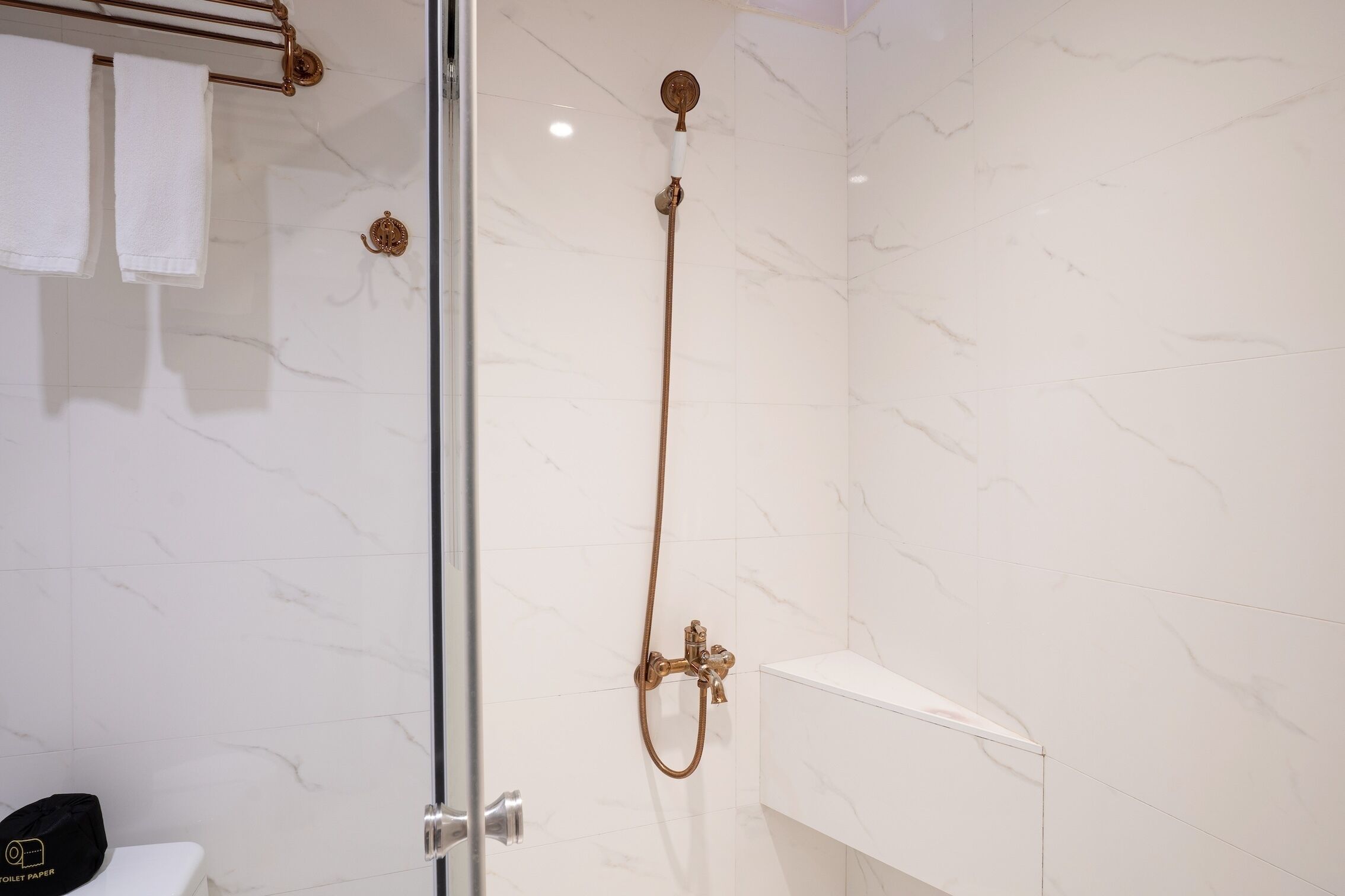 A modern bathroom with a glass-enclosed shower, white marble walls, and a white sink.
