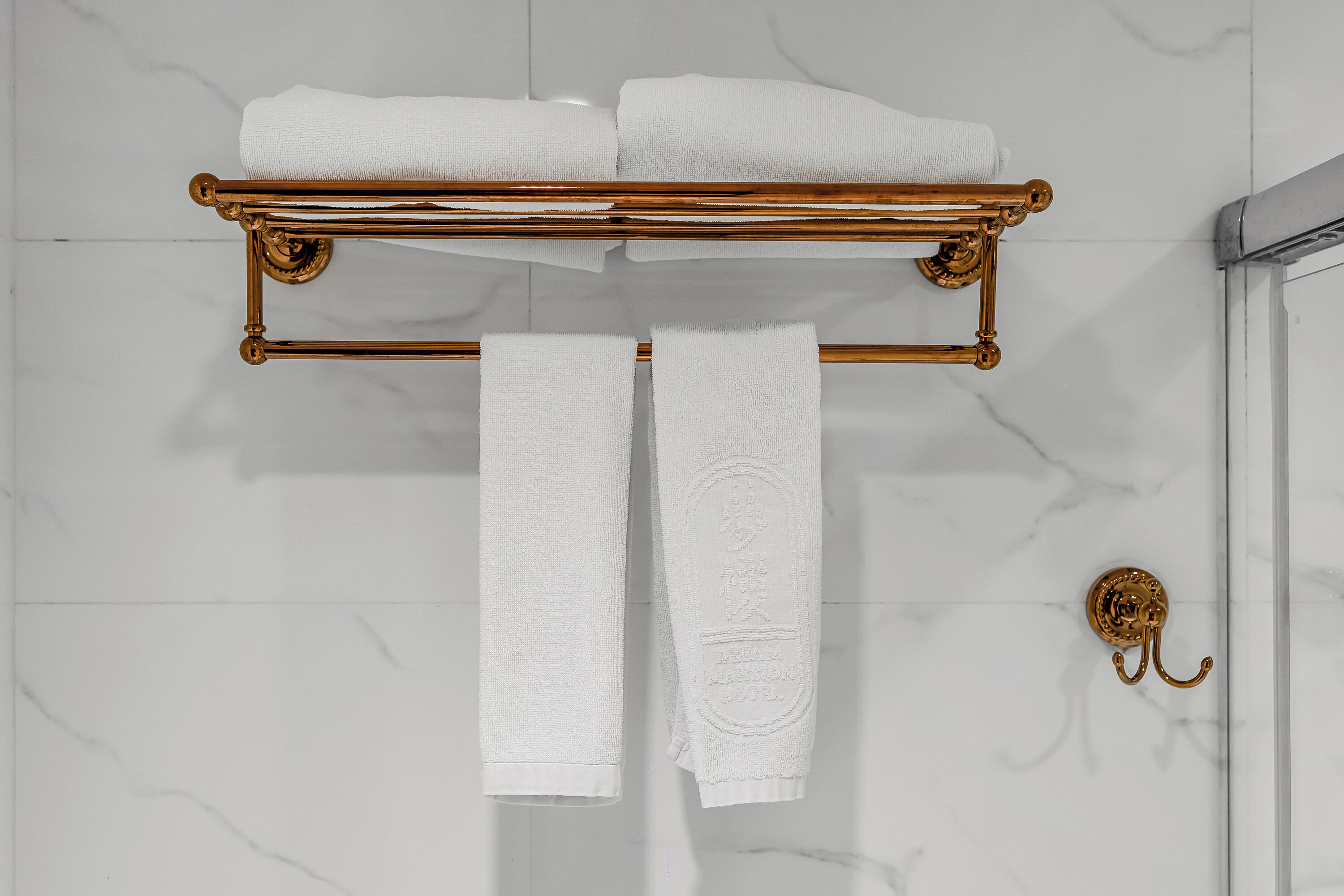 A bathroom with a gold towel rack holding two towels and a gold towel ring on the wall.