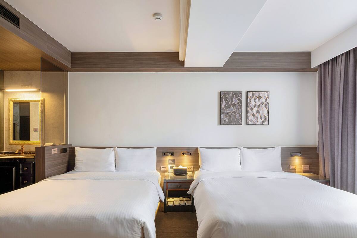 A hotel room with two beds, a mirror, a nightstand, and two wall-mounted lamps.