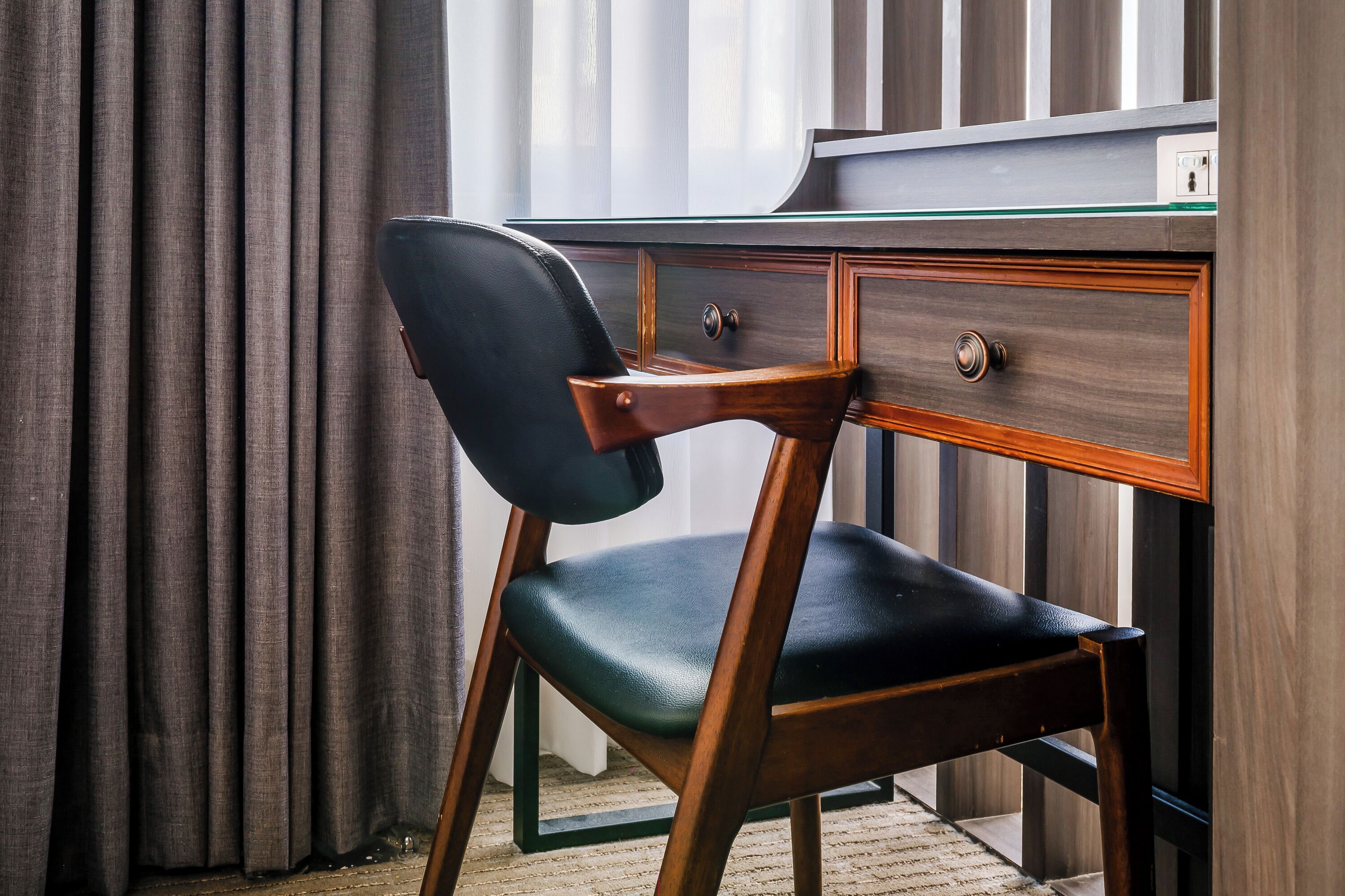 A wooden desk with a black chair, a drawer, and a glass top.