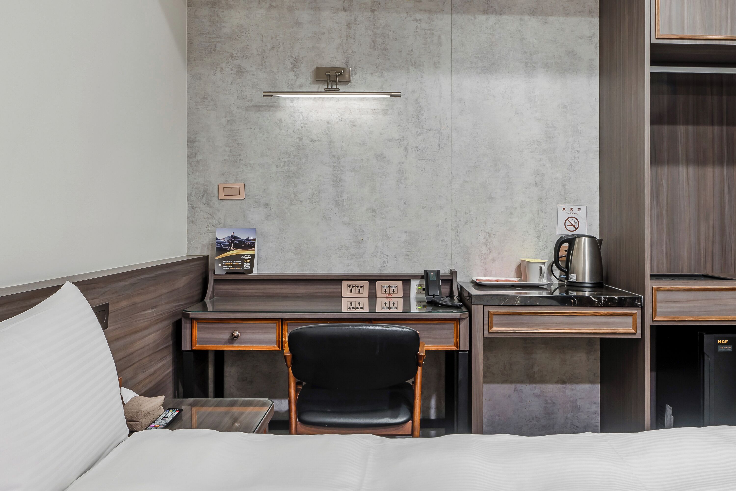 A hotel room with a bed, a desk with a chair, a coffee maker, and a small refrigerator.