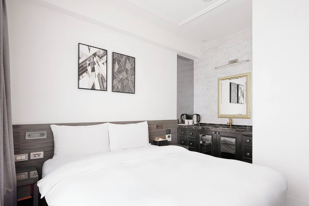 A modern hotel room with a large bed, a vanity with a mirror, and two abstract paintings on the wall.