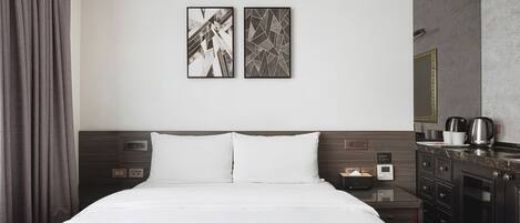 A modern hotel room with a large bed, a nightstand with a lamp, a coffee maker, and a mirror on the wall.