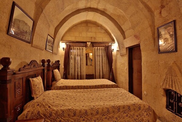 A room with two beds, wooden headboards, and a stone archway. - Travel Inn Cave Hotel (Nevsehir)
