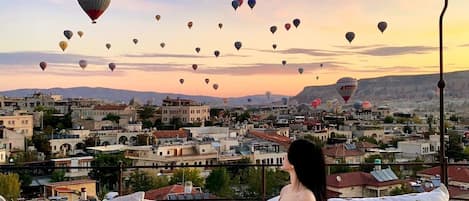 A person sitting on a sofa overlooking a cityscape with numerous hot air balloons in the sky.