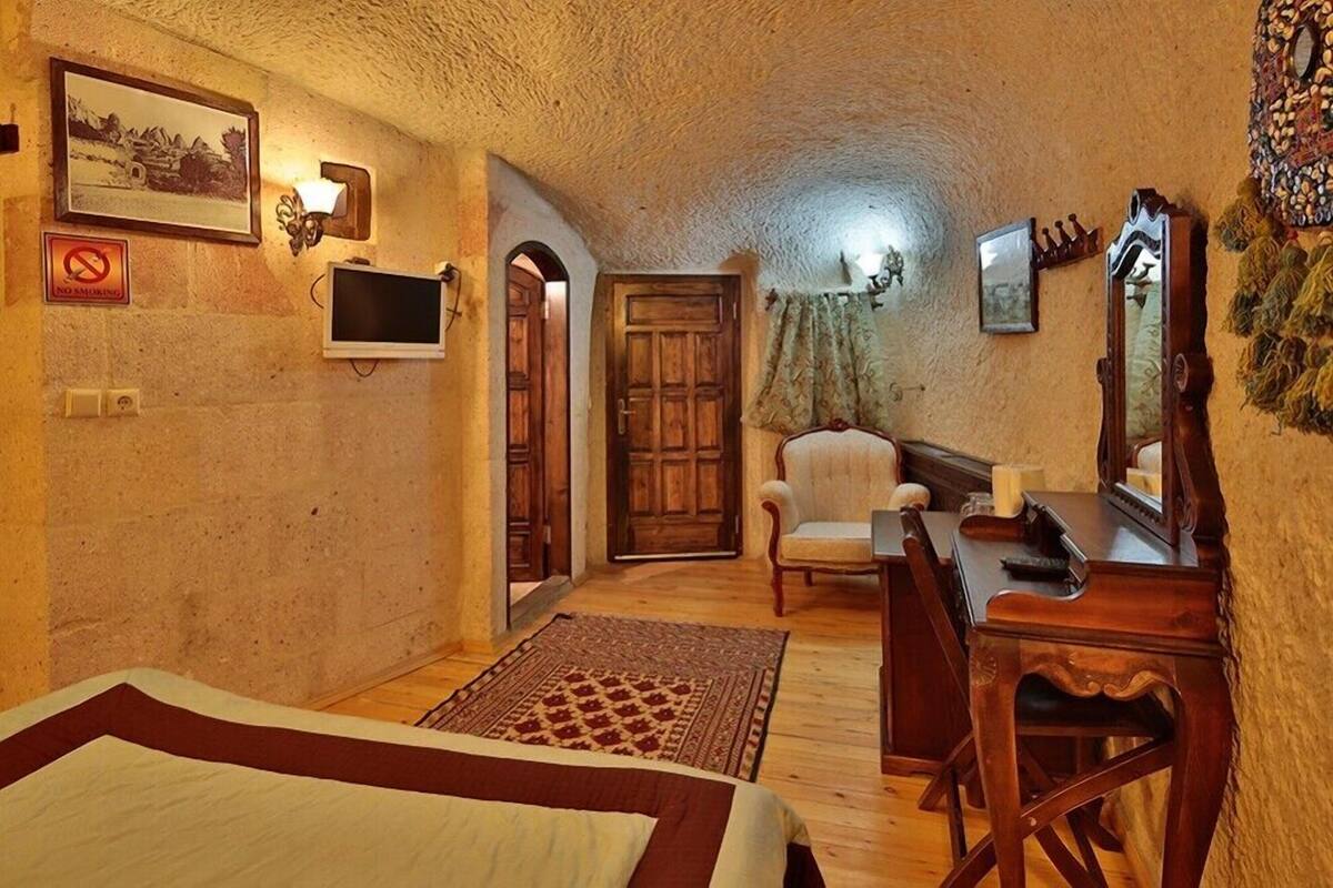 A cozy room with a bed, a desk, a chair, a television, and a door.