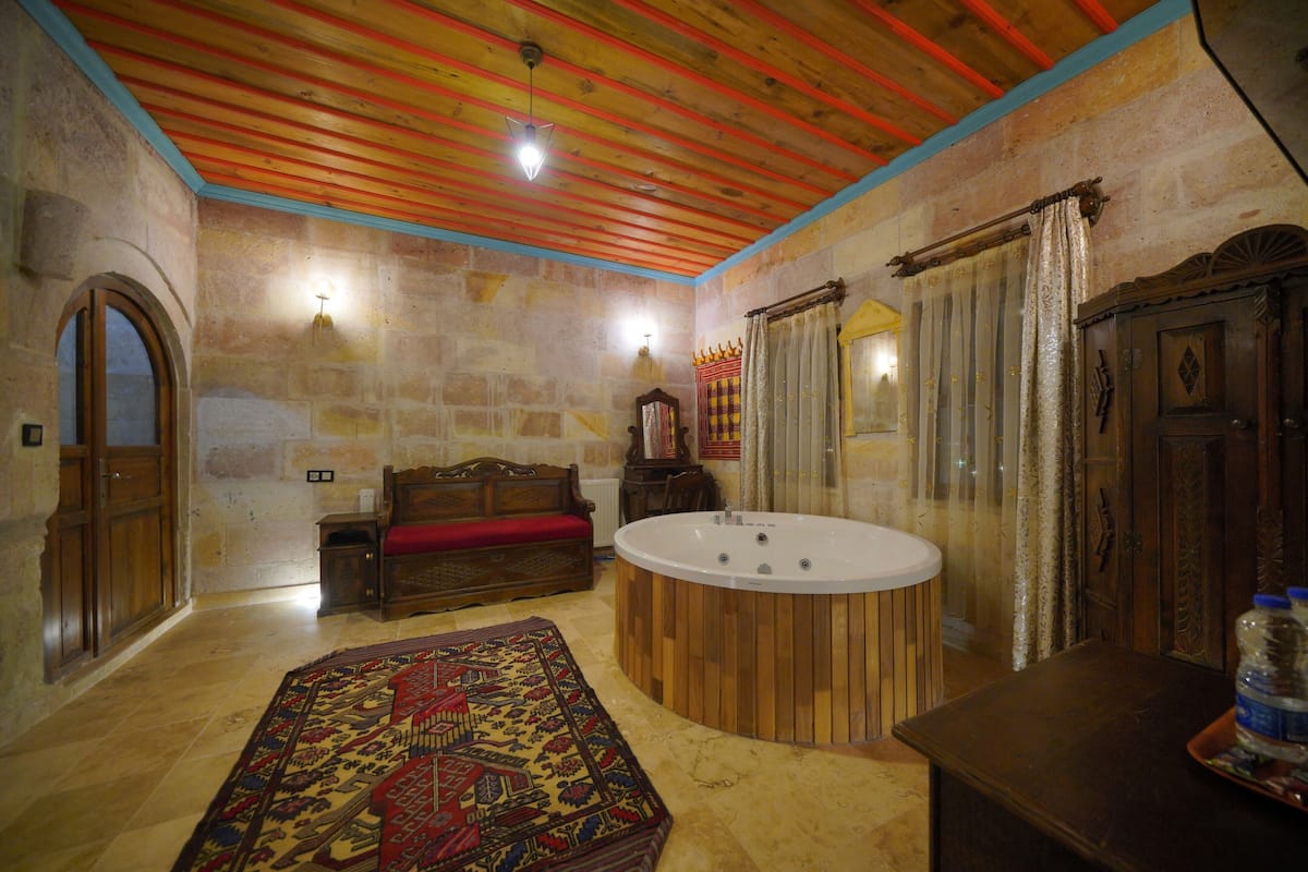 A room with a wooden ceiling, a large wooden bathtub, a red sofa, a patterned rug, and a wooden cabinet.