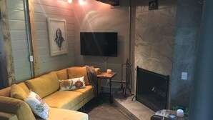 A living room with a yellow sofa, a fireplace, a television, and a stone wall. - Charming 2 Bdrm Condo, Peaceful Setting on Bus Line/Vail #011008 (Vail)