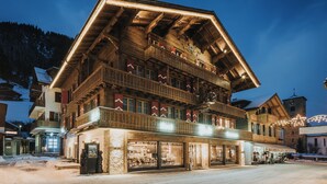 A multi-story wooden building with balconies, a restaurant on the ground floor, and a clock tower in the background. - Hotel Bären (Adelboden)