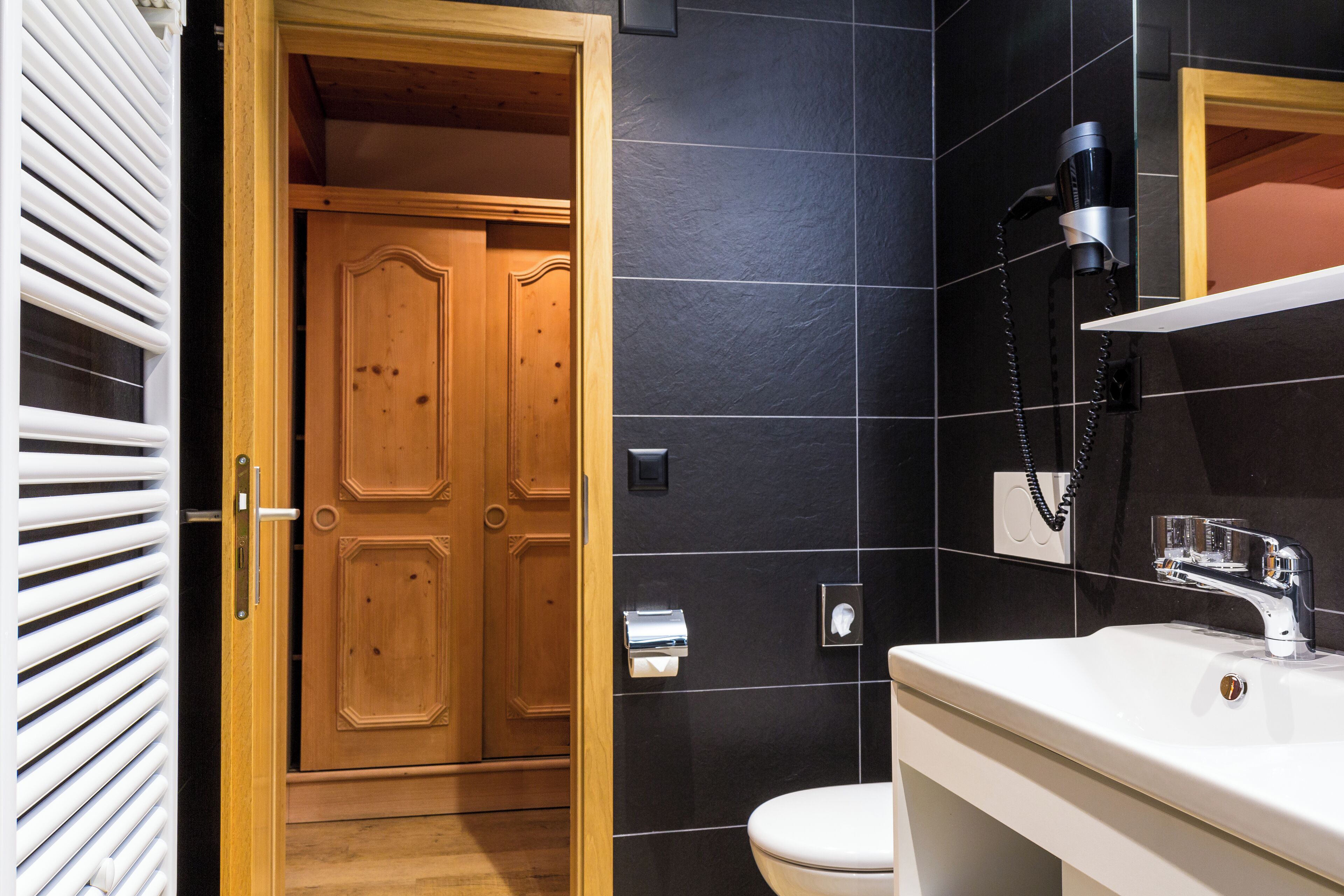 A bathroom with a wooden door, a white sink, and a black tiled wall.