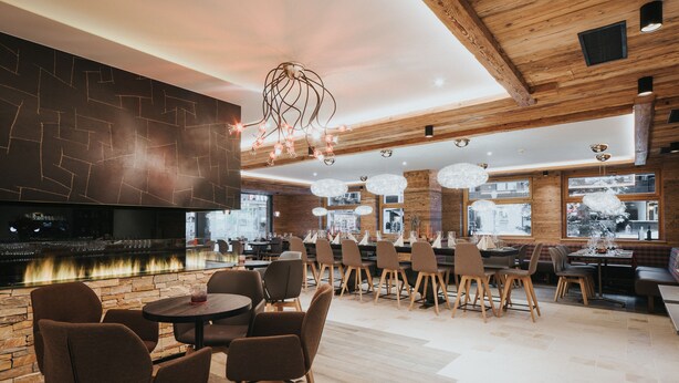 A modern restaurant with a bar area, wooden ceiling, and large windows. - Hotel Bären (Adelboden)