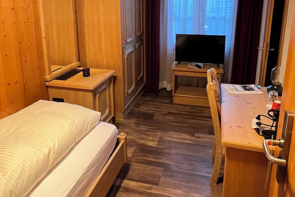 A wooden room with a bed, a desk, a television, and a wardrobe.