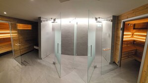 A modern bathroom with glass-enclosed shower stalls, wooden paneling, and a tiled floor. - Hotel Bären (Adelboden)