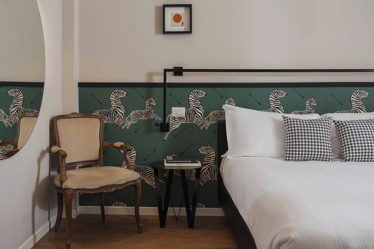 Ein Schlafzimmer mit einem zebraartig gestreiften Kopfteil, einem hölzernen Stuhl, einem Nachttisch und einem gerahmten Bild an der Wand.
