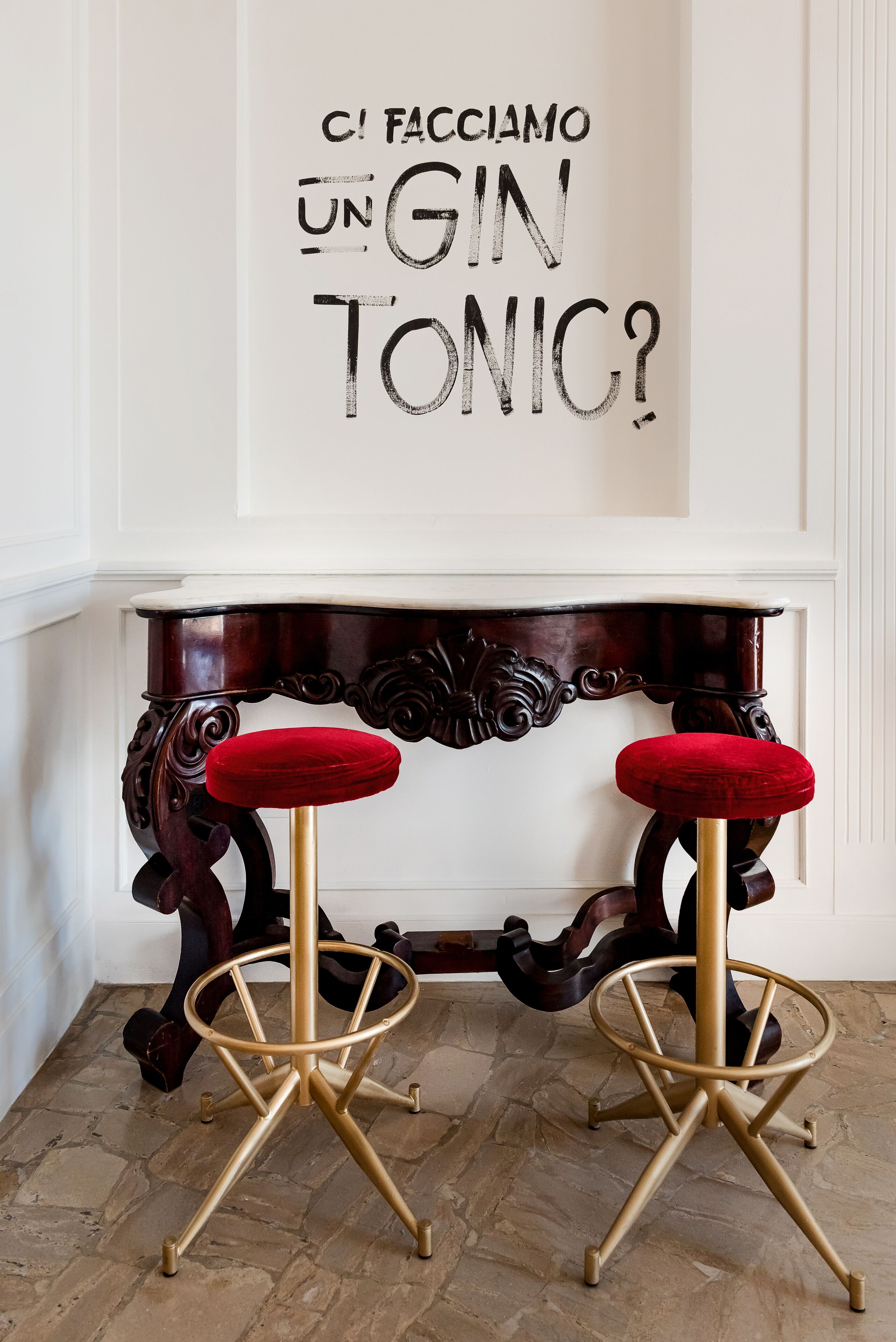 Um espaço de bar com uma mesa de console decorativa e dois banquetes com almofadas vermelhas.