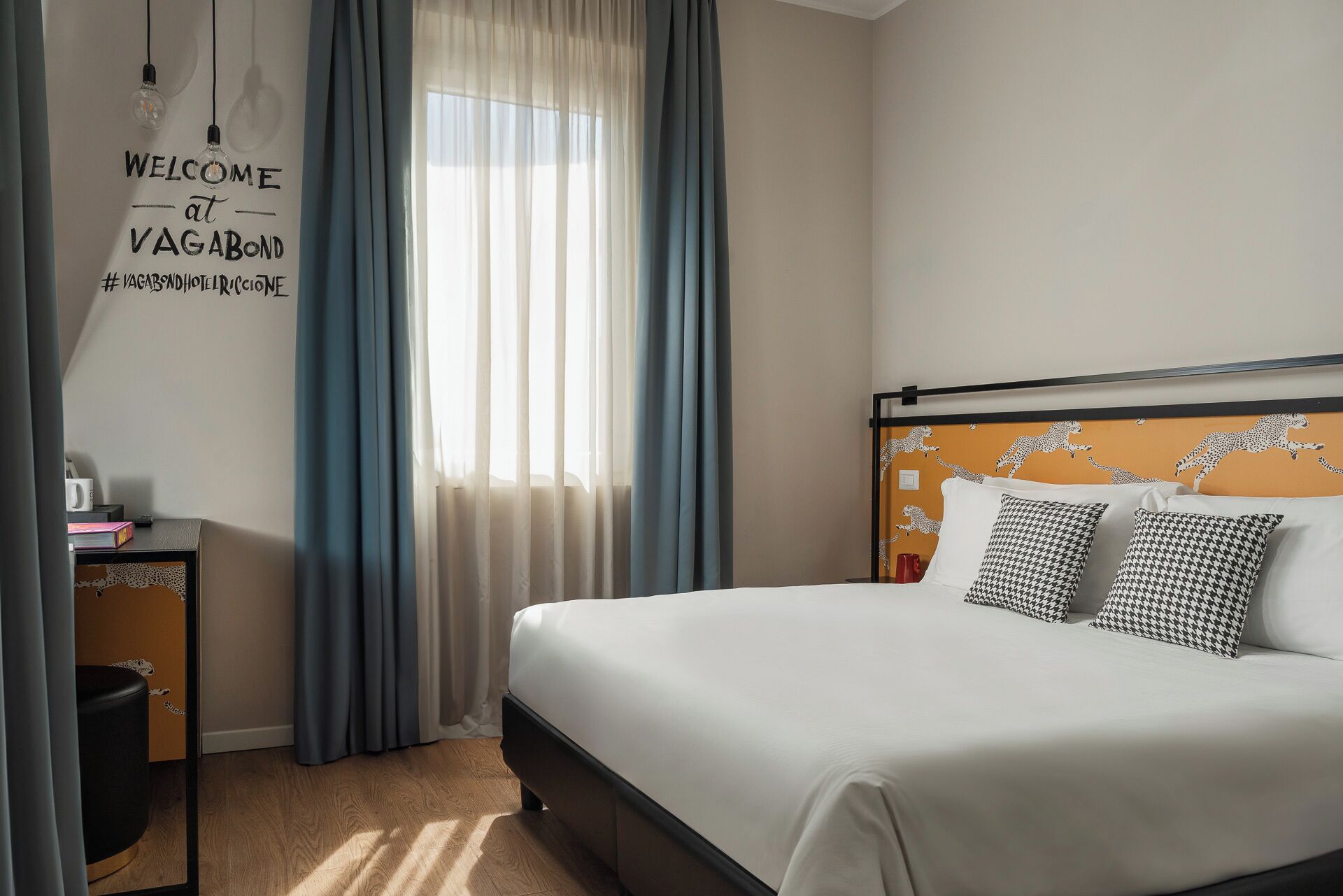 A hotel room with a bed, a desk, a chair, and a window with curtains.