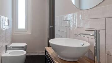 A modern bathroom with a large vessel sink, a toilet, and a shower.