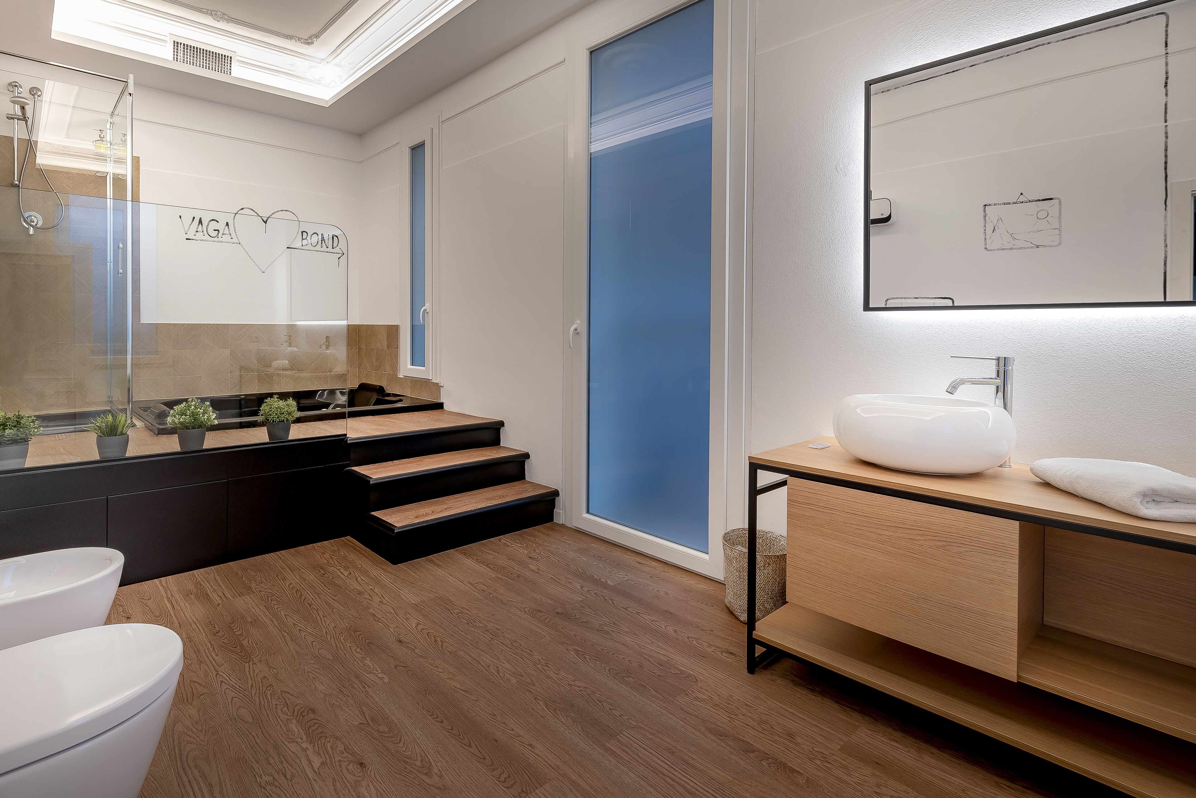 Een moderne badkamer met een houten vloer, een witte wastafel en een douchecabine met glazen wanden.
