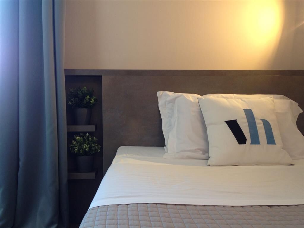 Una cama bien hecha con ropa de cama blanca y dos almohadas, una con la letra 'h' en azul.